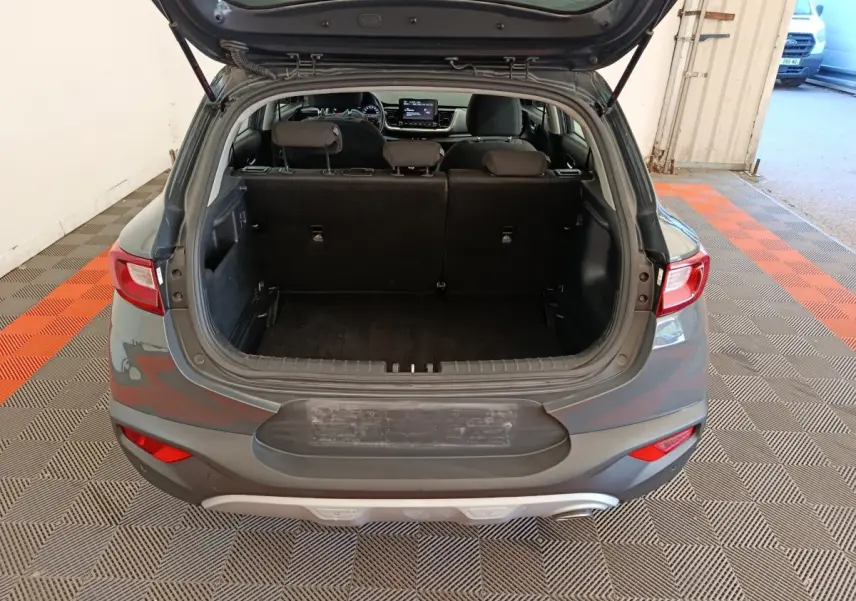 Vue arrière ouverte du coffre d'un KIA STONIC gris foncé 2023, montrant l'espace intérieur et les sièges rabattus.