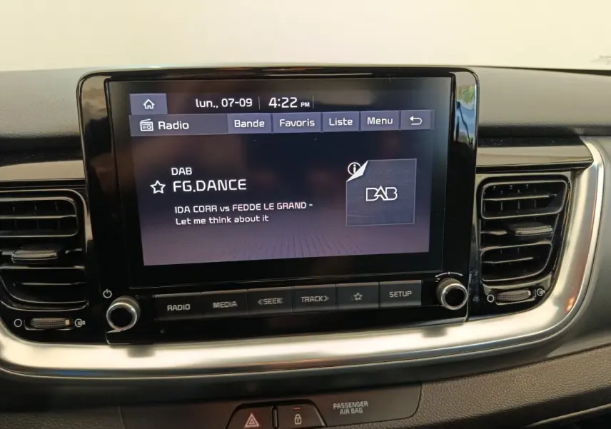 Écran tactile central de la Kia Stonic 1.0 T-GDI 2023 affichant une station radio DAB, entouré de grilles d'aération noires.