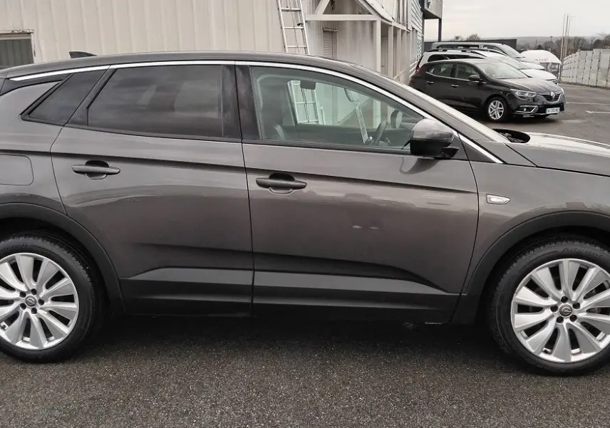 Vue de profil côté gauche d'un Opel Grandland X gris platinium avec jantes alliage et vitres teintées, stationné en extérieur.
