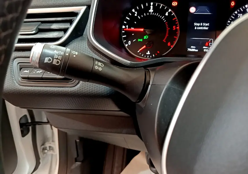 Gros plan sur la manette des phares et clignotants à gauche du volant d'une Renault Clio Business Blue dCi 85 blanche, tableau de bord visible.