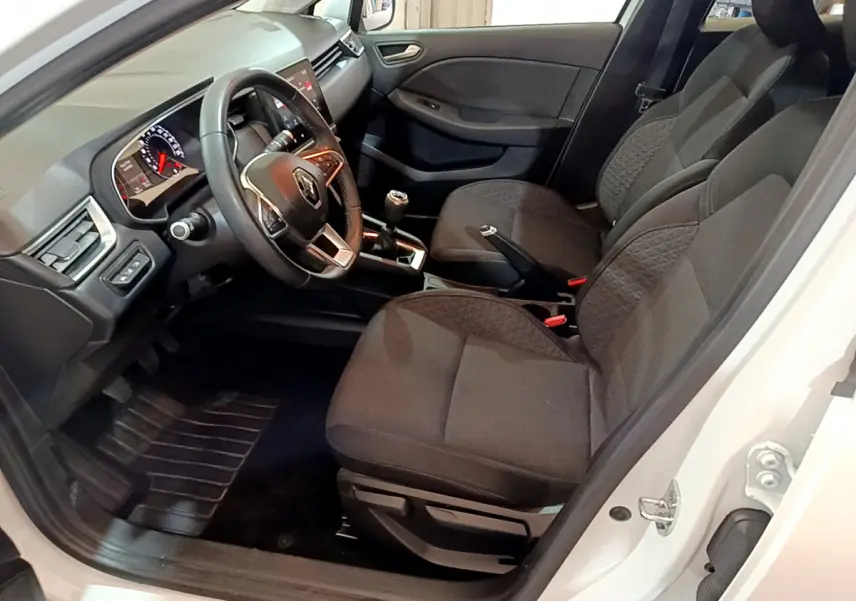 Intérieur côté conducteur d'une Renault Clio Business blanc, volant cuir, sièges tissu gris et tableau de bord moderne.