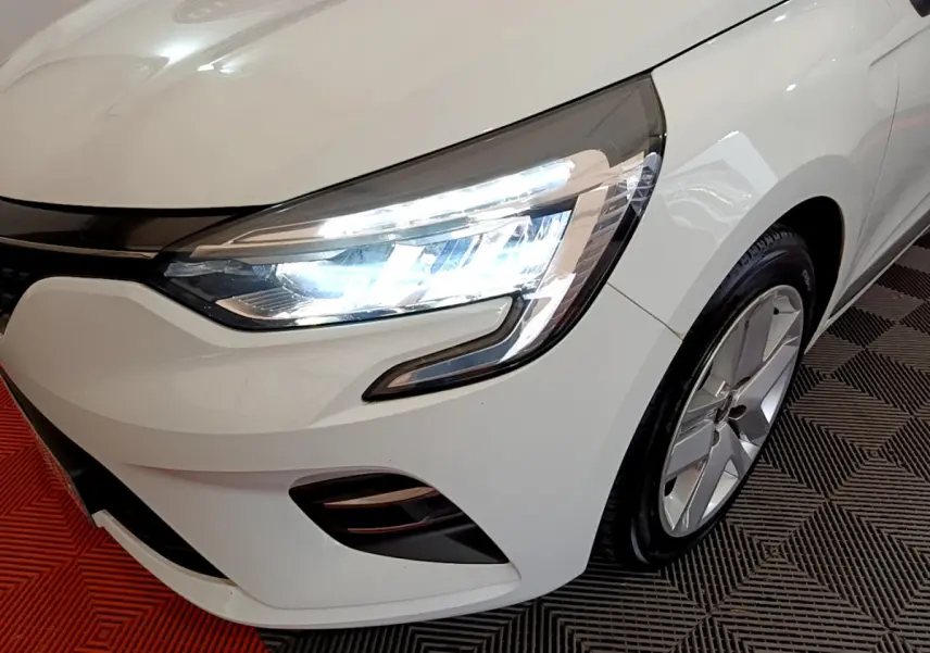 Gros plan sur l'avant droit blanc d'une Renault Clio 2020 avec phare LED allumé et jante alliage visible