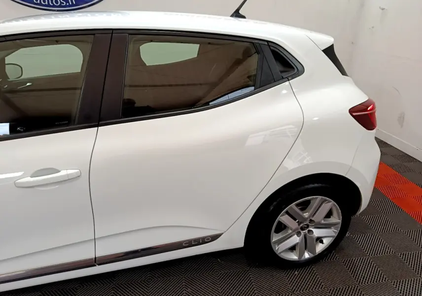 Vue latérale côté droit d'une Renault Clio blanche avec jante alliage et logo Clio sur la bas de porte arrière.
