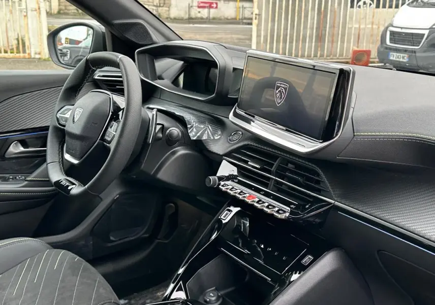 Vue intérieure côté conducteur du Peugeot 208 Hybrid 110 gris, mettant en valeur le volant GT, l'écran tactile et la finition moderne du tableau de bord.