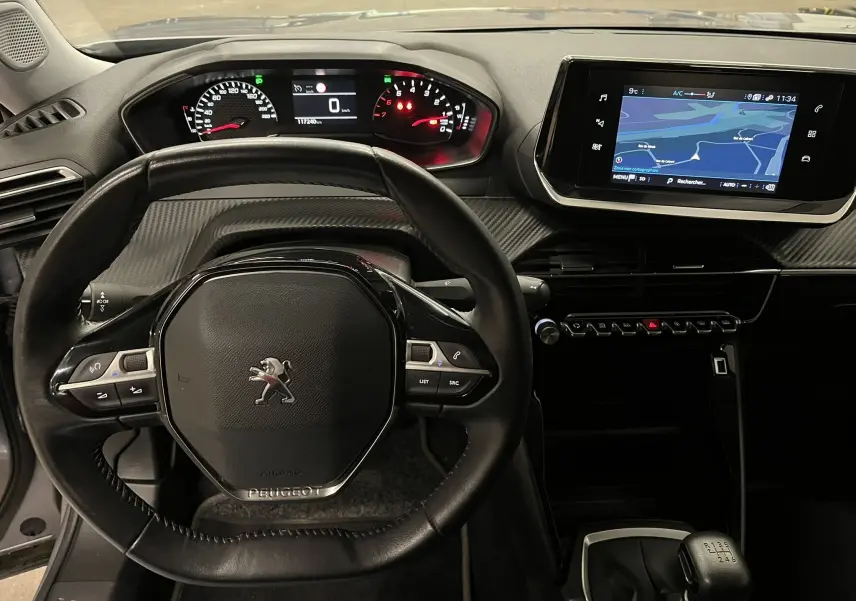 Vue intérieure du tableau de bord du Peugeot 2008 gris alu, avec volant multifonction et écran tactile de navigation allumé.