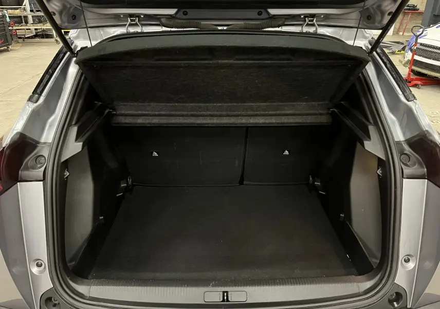 Coffre ouvert vu de l'arrière d'un Peugeot 2008 gris alu, montrant l'espace de chargement vide et la tablette arrière relevée.