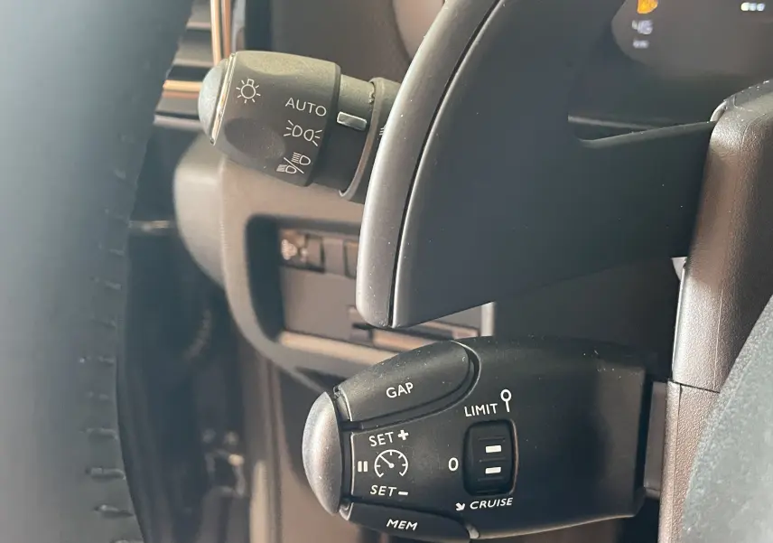 Gros plan sur la commande de régulateur de vitesse au volant d’un Citroën C5 Aircross hybride gris platinium, intérieur noir.