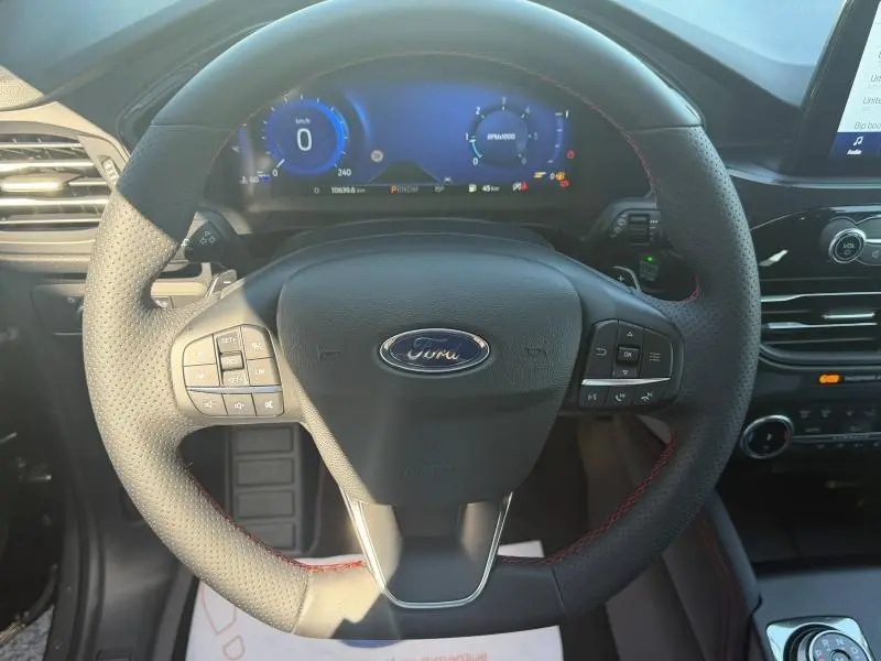 Vue intérieure centrée sur le volant cuir multifonction du Ford Kuga 2024 avec tableau de bord numérique bleu.