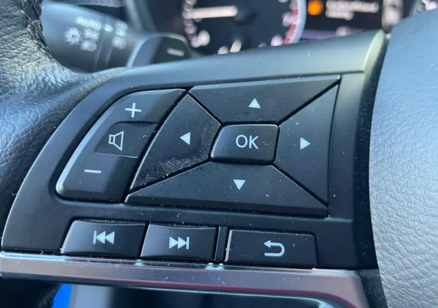 Gros plan sur les commandes au volant noir du Nissan Juke II 2024 en bleu Magnetic, avec boutons multifonctions.