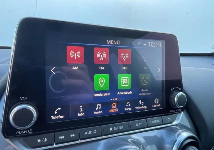 Écran tactile central du Nissan Juke II 2024 affichant le menu multimédia avec commandes autour, intérieur noir.