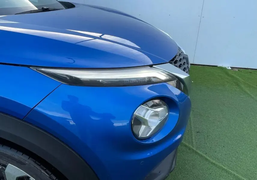 Gros plan sur l'avant droit du Nissan Juke II 2024 en bleu magnetic, mettant en valeur ses phares LED et la calandre noire.