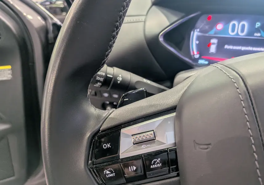 Gros plan sur le volant cuir noir du DS3 2024 gris Platinium, avec commandes intégrées et tableau de bord numérique en arrière-plan.