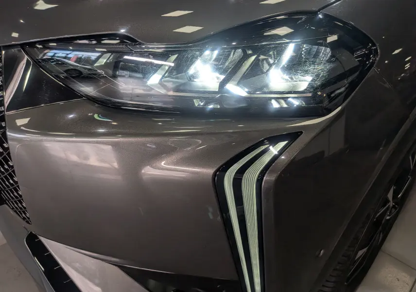 Gros plan sur le phare avant droit allumé d'une DS3 2024 gris Platinium avec feux LED distinctifs en forme de flèche.