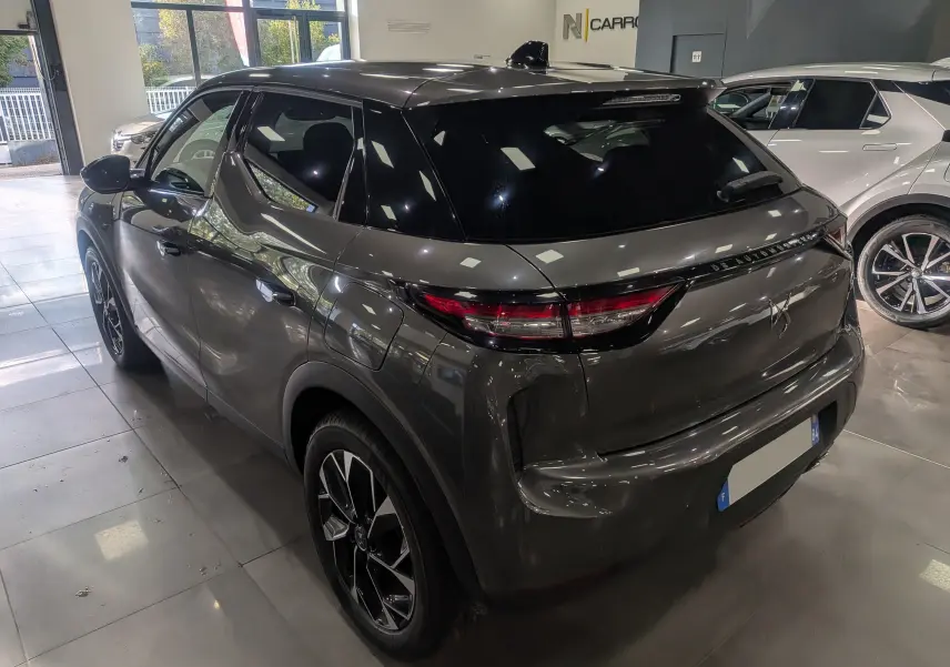 Vue 3/4 arrière droite d'un DS3 2024 gris Platinium avec toit noir brillant et feux arrière effilés en intérieur showroom.