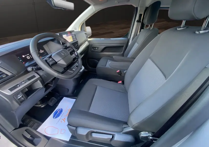 Intérieur avant du Citroën Jumpy XL gris acier, sièges tissu bi-ton noir-gris avec accoudoirs et tableau de bord moderne.