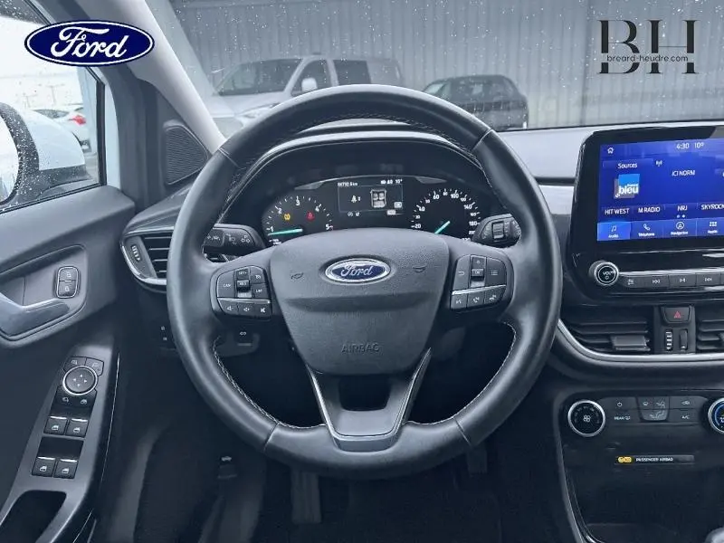 Vue intérieure centrée sur le volant cuir multifonction d'une Ford Puma blanc Glacier avec écran tactile et commandes au volant.