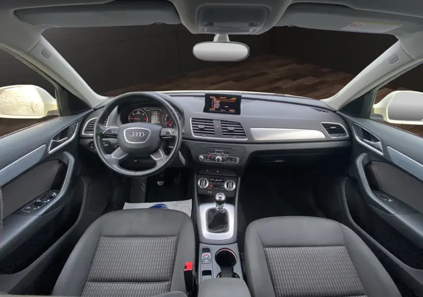 Vue intérieure avant de l'Audi Q3 2.0 TDI 2014 avec tableau de bord noir, volant cuir et écran GPS central.
