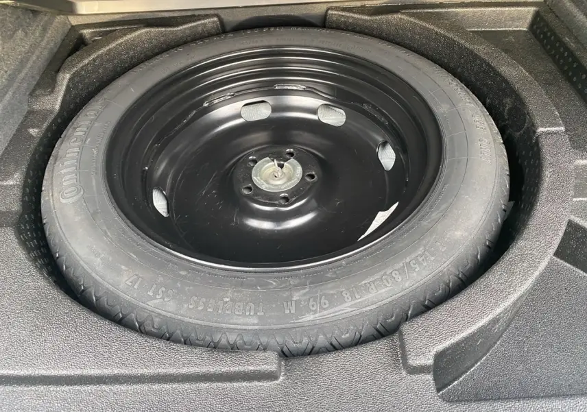 Roue de secours noire dans le coffre d’un Audi Q3 blanc, vue en plongée sur le pneu Continental.