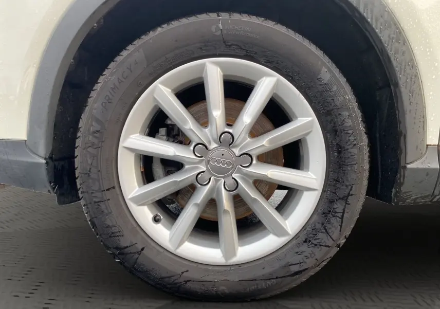 Gros plan sur la roue avant droite blanche d’un Audi Q3 2.0 TDI avec jante argentée à 10 branches.