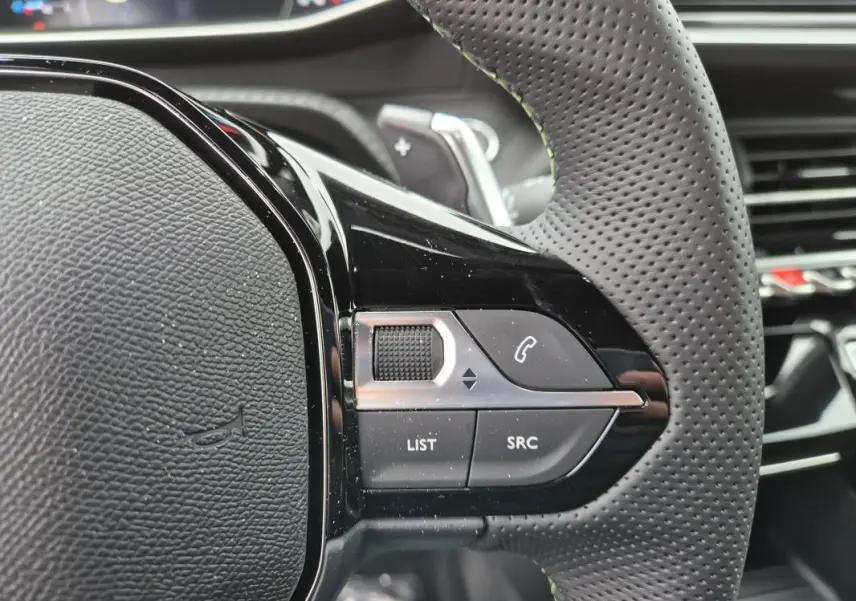 Gros plan sur le volant perforé de la Peugeot 208 Hybrid 110 e-DCS6 GT gris, avec commandes audio et téléphone intégrées.