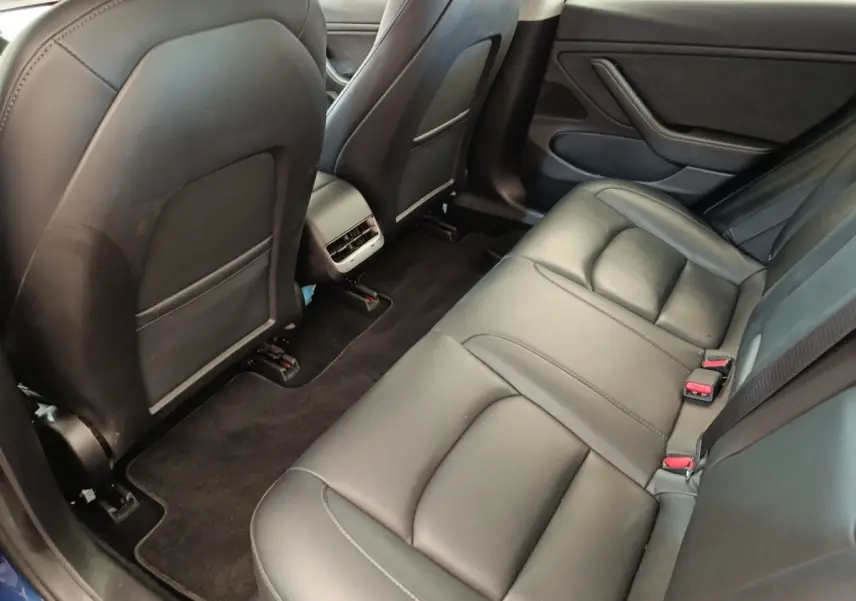 Vue intérieure côté arrière droit montrant la banquette en cuir noir et les dossiers des sièges avant d'une Tesla Model 3 bleu.