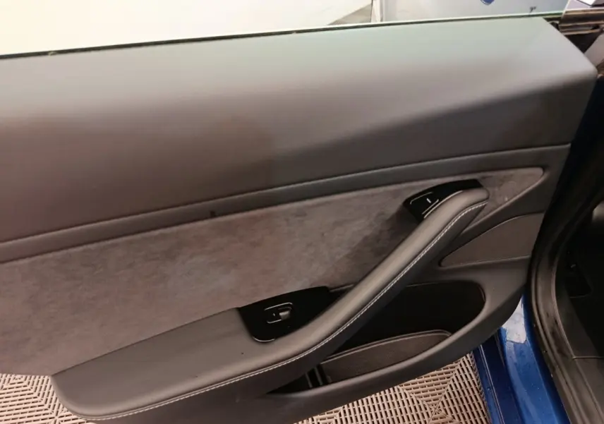 Vue intérieure du panneau de porte côté gauche d'une Tesla Model 3 bleu, avec accoudoir en cuir et commande de fenêtre.