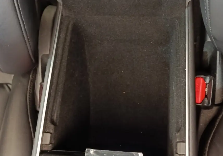 Vue rapprochée de la console centrale ouverte d'une Tesla Model 3 Long Range bleu, montrant un compartiment vide et un manuel.