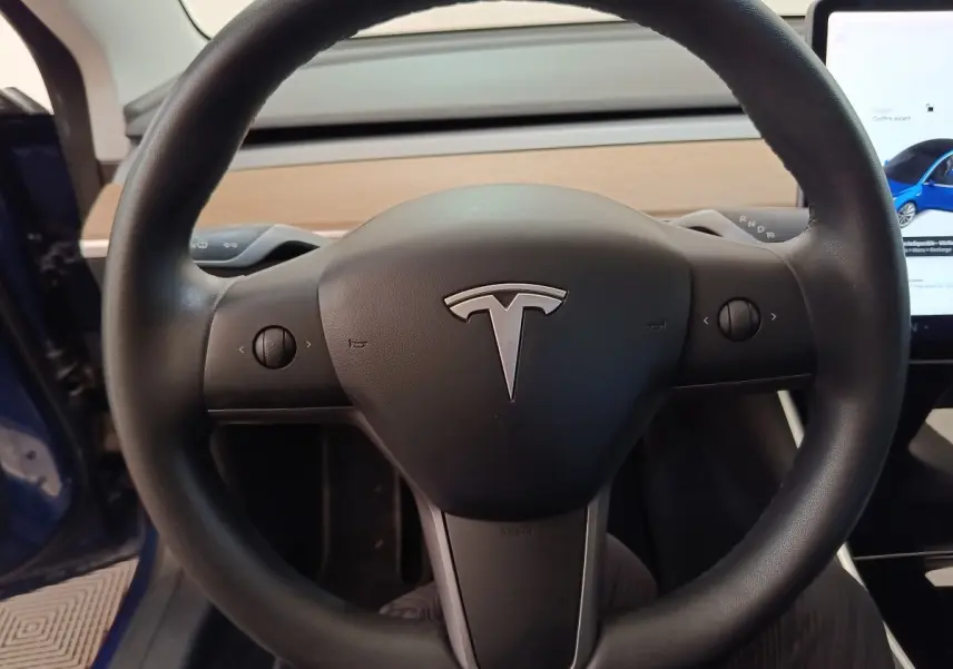 Vue rapprochée du volant noir de la Tesla Model 3 Long Range 2020 avec tableau de bord en bois clair visible.