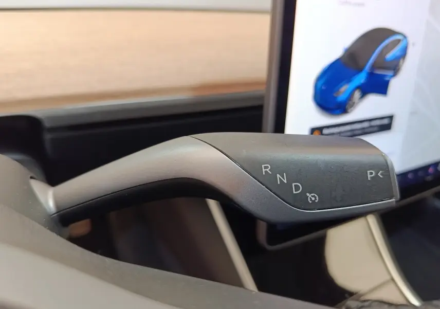 Le levier de vitesses automatique de la Tesla Model 3 Long Range, vue rapprochée à l'intérieur, avec écran tactile en arrière-plan.