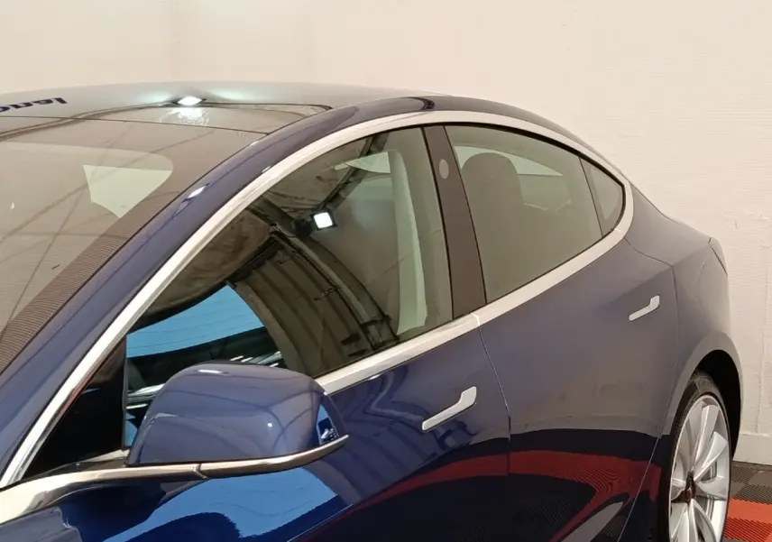 Vue côté gauche rapprochée d’une Tesla Model 3 Long Range bleu, mettant en valeur la ligne fluide et les rétroviseurs électriques.