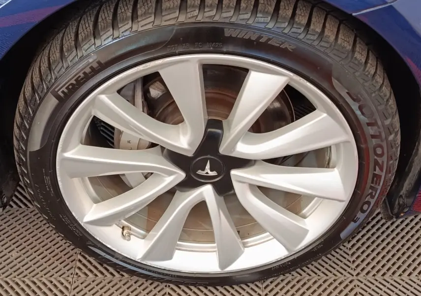 Gros plan sur la roue avant droite d'une Tesla Model 3 bleu, jante argentée avec logo Tesla au centre.