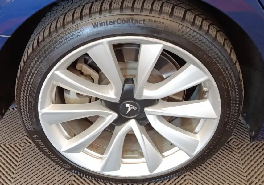 Gros plan sur la roue avant droite d’une Tesla Model 3 bleu, avec jante argentée et pneu hiver Continental.