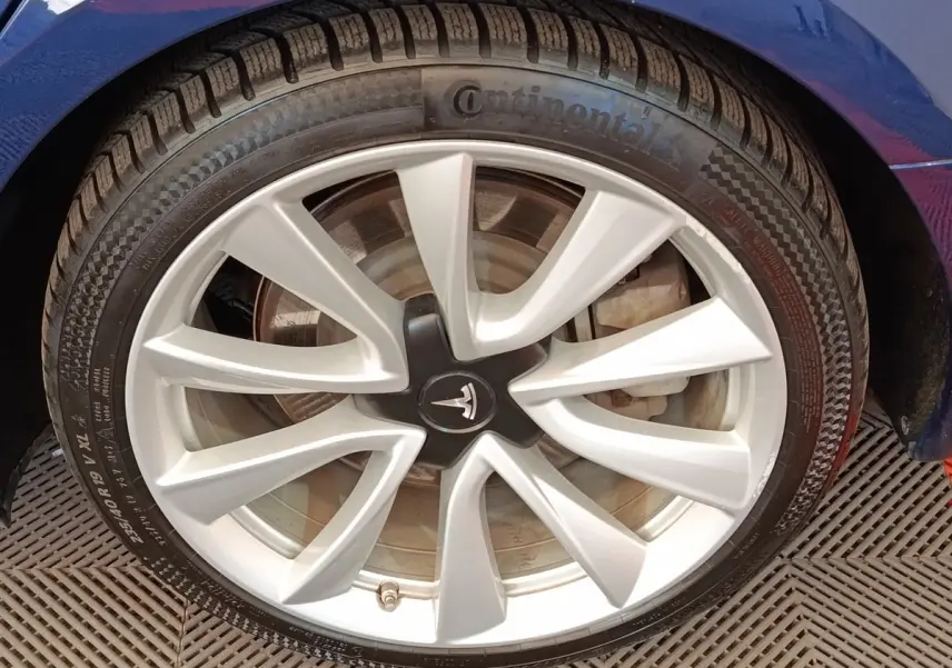 Gros plan sur la roue avant gauche d’une Tesla Model 3 Long Range bleu avec jante argentée et logo Tesla au centre.