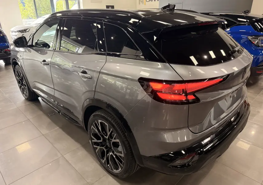 Vue 3/4 arrière droite du Renault Austral gris schiste avec toit noir et feux arrière allumés en intérieur showroom.