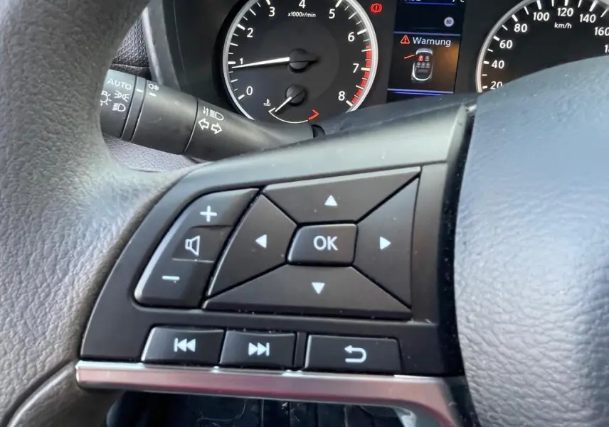 Gros plan sur les commandes au volant à gauche du Nissan Juke II gris Ceramic, avec compte-tours et écran digital en arrière-plan.