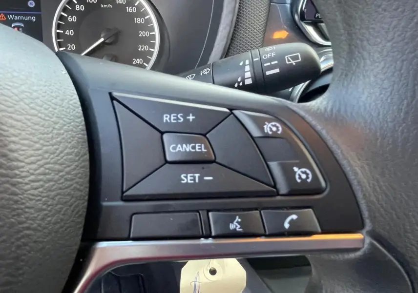 Gros plan sur les commandes noires du régulateur de vitesse au volant cuir du Nissan Juke gris Ceramic 2024