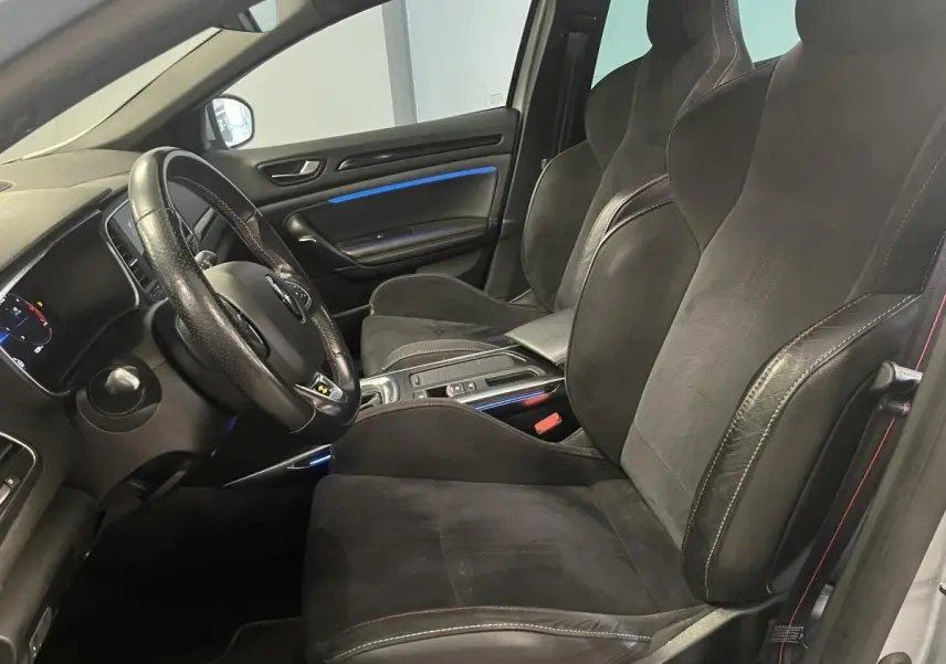 Intérieur avant de la Renault Mégane gris Highland, sièges sport Alcantara noirs avec surpiqûres rouges et éclairage d'ambiance bleu.