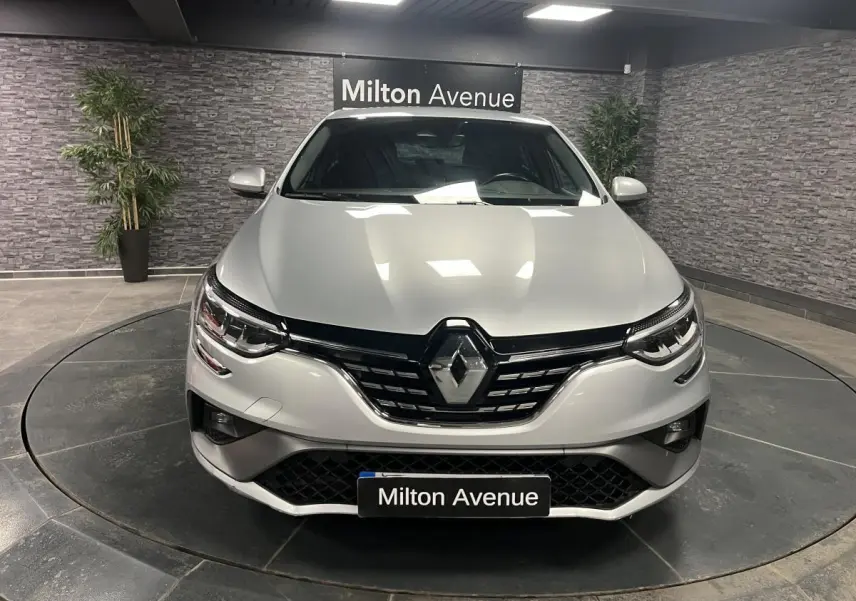 Vue frontale d'une Renault Mégane gris Highland avec calandre noire et logo chromé, en showroom intérieur.