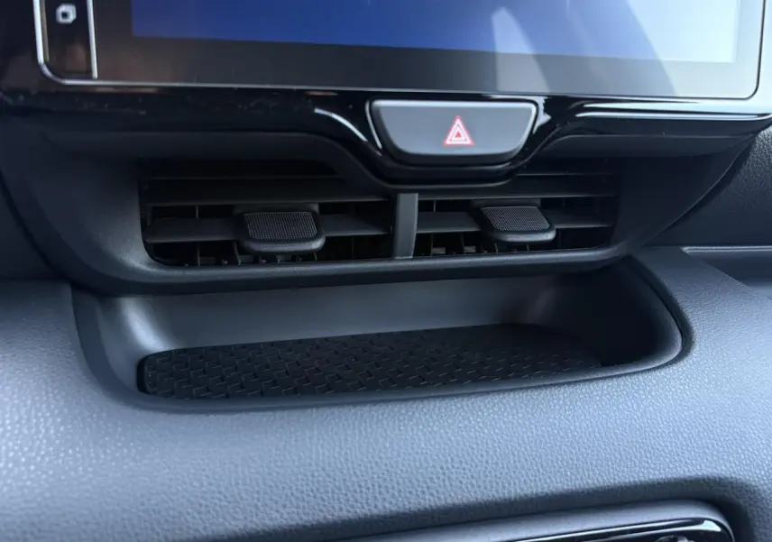 Gros plan sur la console centrale noire de la Toyota Yaris hybride 2025, avec les aérateurs et le bouton de warning visible.