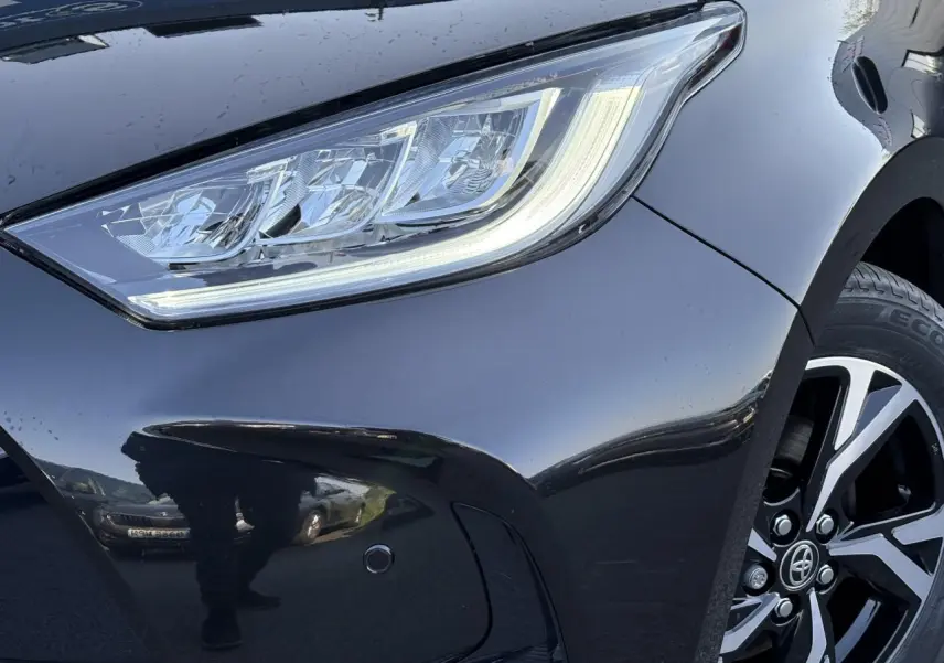 Gros plan sur le phare avant droit et la jante alliage 16'' d'une Toyota Yaris Hybride 2025 noir intense.