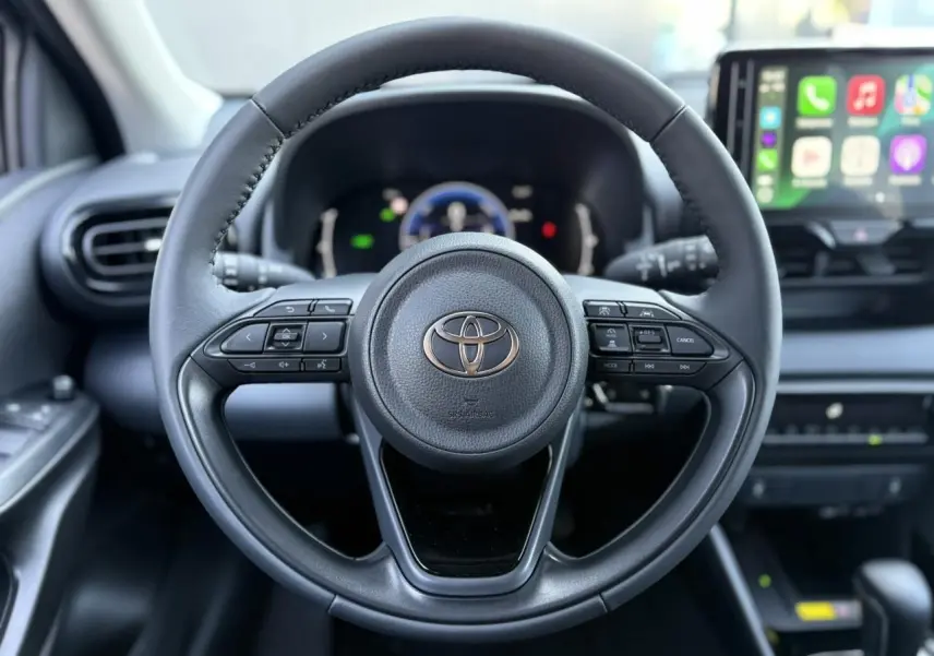 Vue centrée sur le volant cuir noir de la Toyota Yaris 2025 hybride, avec tableau de bord numérique et écran tactile visible.