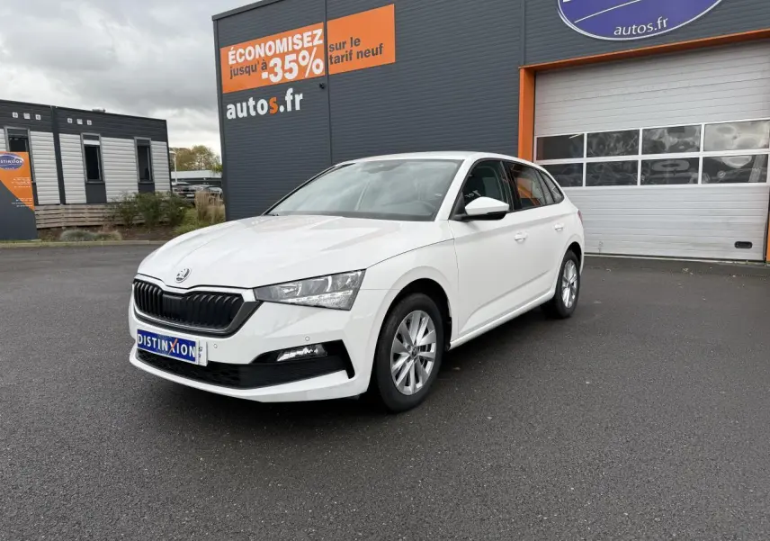 Vue 3/4 avant d'une Skoda Scala blanche stationnée devant un bâtiment commercial avec jantes alliage argent.