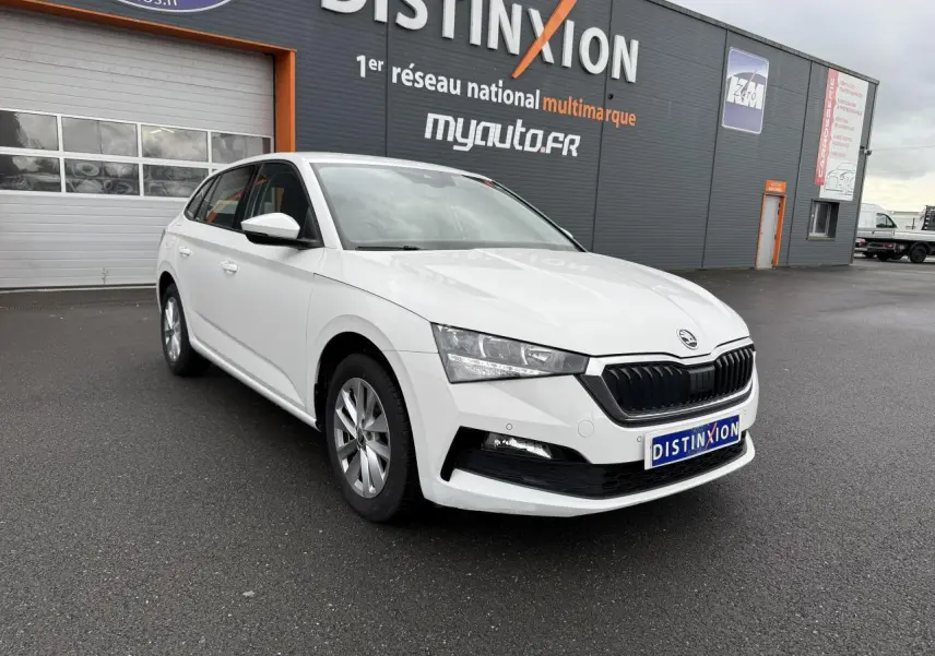 Vue 3/4 avant d'une Skoda Scala blanche 2023 avec jantes alliage argent devant un bâtiment gris.