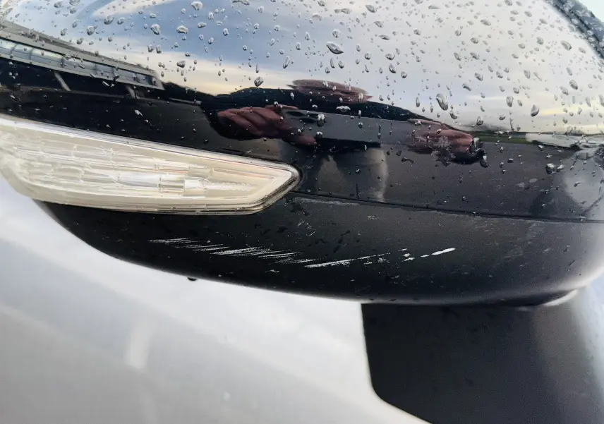 Gros plan sur le rétroviseur droit noir brillant avec clignotant intégré et traces de rayures sur une Citroën C3 Aircross gris Artense.