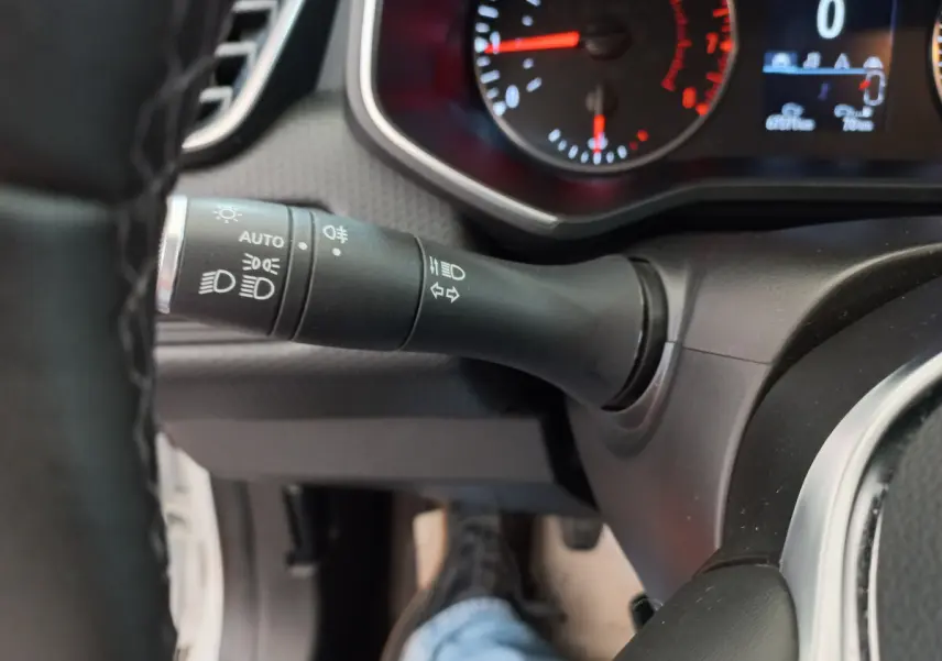 Gros plan sur la manette des feux à gauche du volant d'une Renault Clio Business blanche, tableau de bord partiellement visible.