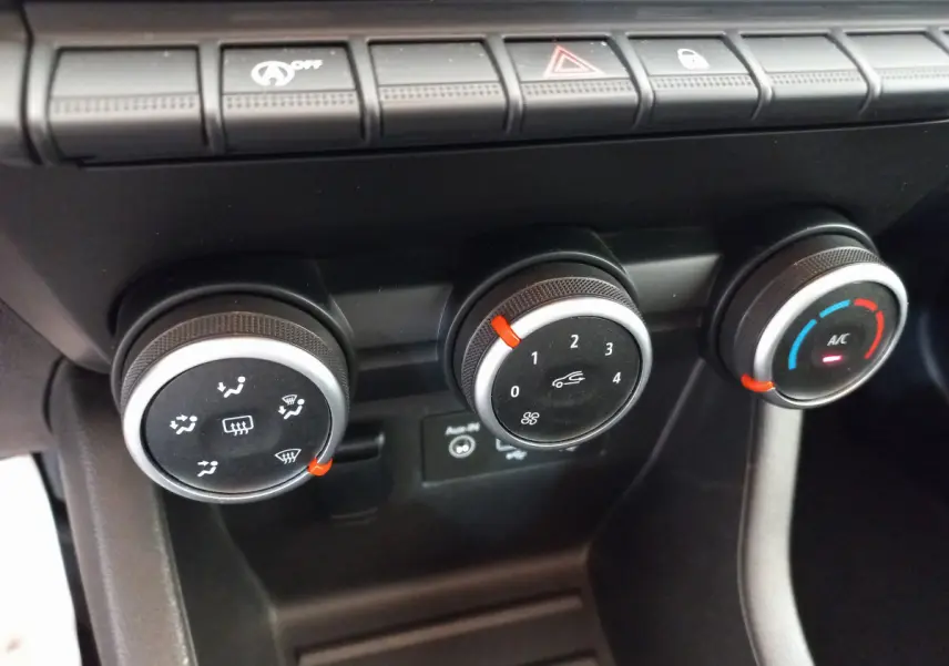 Gros plan sur les commandes de climatisation de la Renault Clio Business blanche, boutons noirs avec indicateurs rouges et bleus.