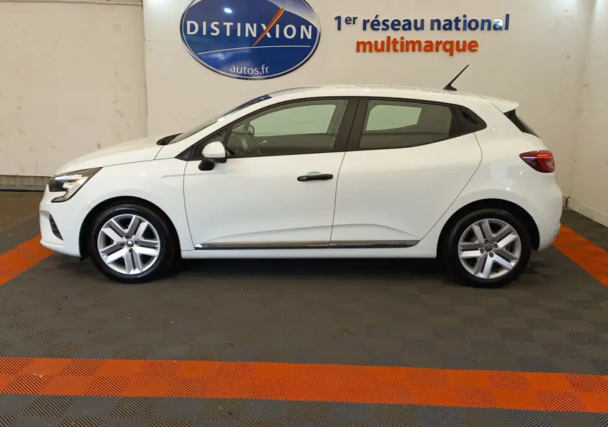 Profil côté gauche d'une Renault Clio Business blanche 2021, avec jantes alliage et poignées noires visibles en intérieur showroom.