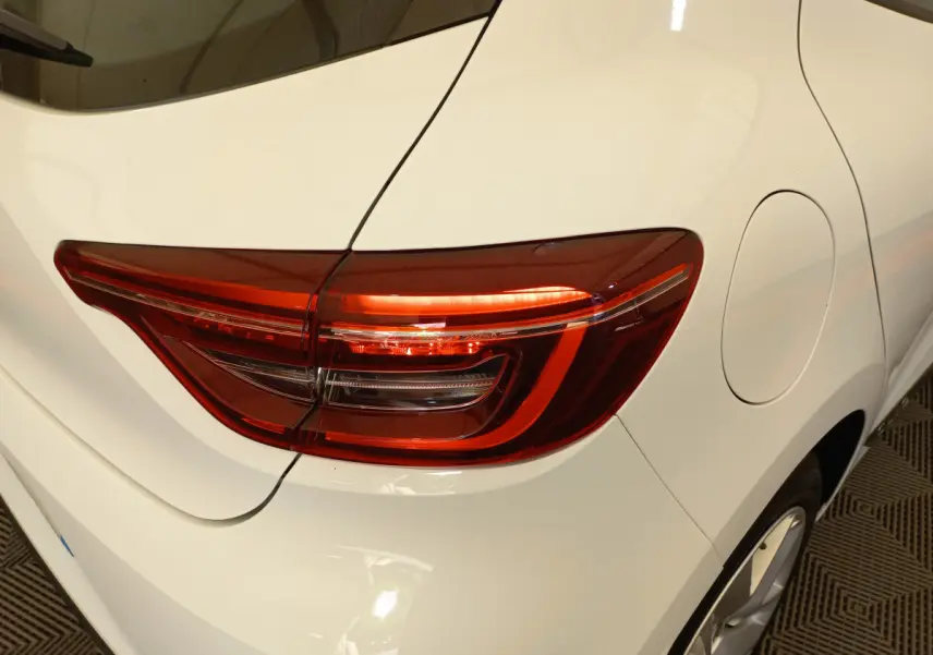 Gros plan sur le feu arrière droit rouge d'une Renault Clio blanche, avec la trappe à carburant visible sur le côté.