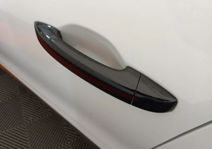 Poignée de porte noire en gros plan sur la portière blanche côté gauche d'une Renault Clio Business 2021.