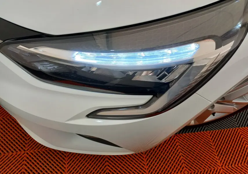 Gros plan sur le phare avant droit blanc d'une Renault Clio Business 2021, avec éclairage LED allumé sur sol orange.